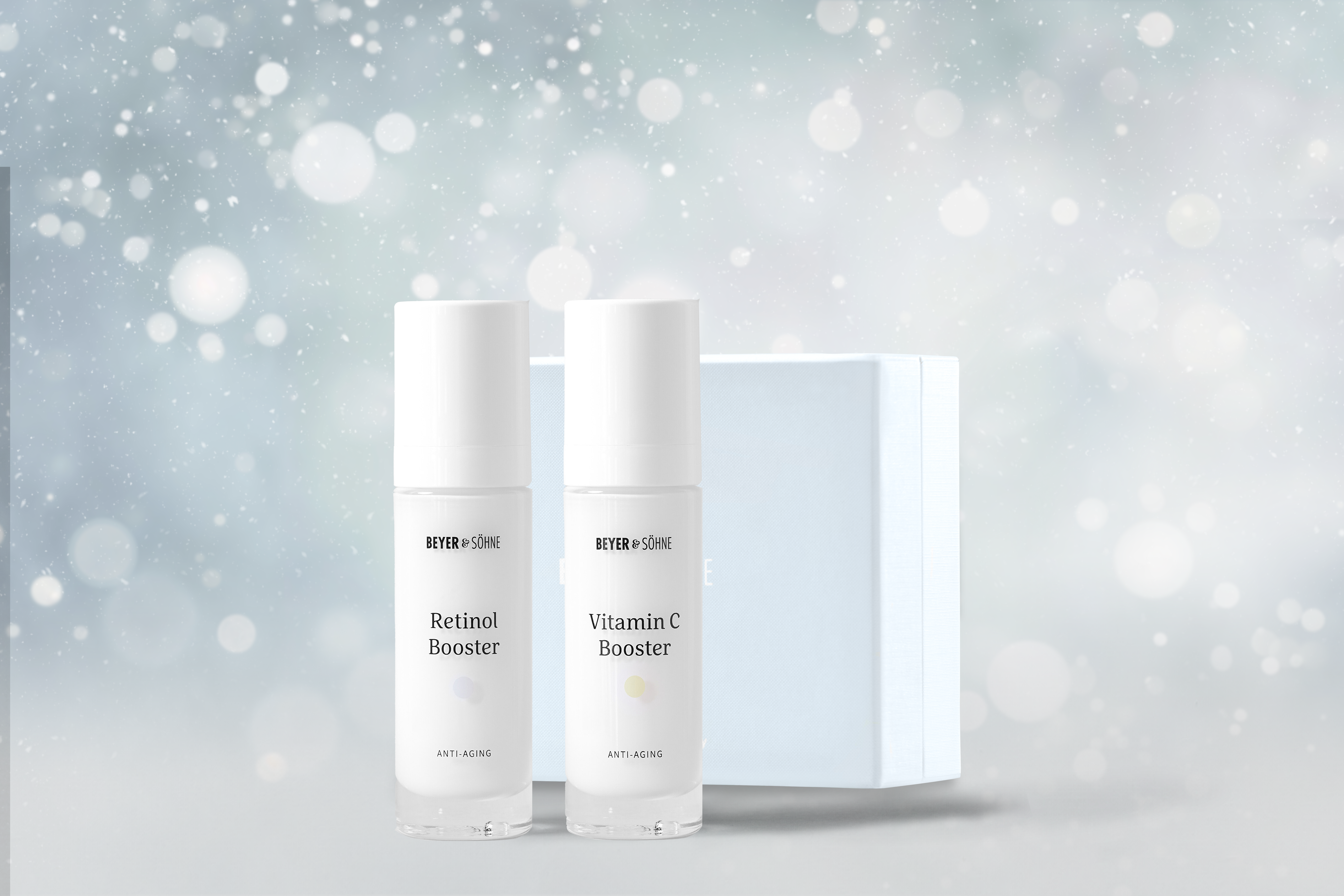 Retinol Booster und Vitamin C Booster in hochwertigen Glasspendern von Beyer & Söhne vor himmelblauer Geschenkbox und weihnachtlich gestimmten Hintergrund mit Schneeflocken.